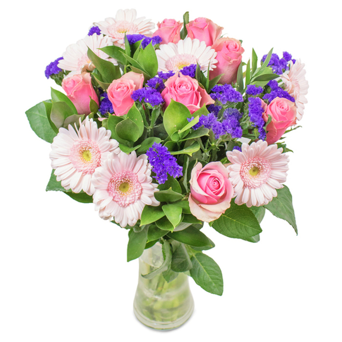 This vibrant, professionally arranged bouquet rests in a classic clear glass vase, set plainly against a pristine white background-an elegant sight familiar in many Stockwell homes and studios. The focal point is a harmonious gathering of approximately seven to nine medium pink roses, some tightly furled and others gently blooming into classic spirals, their delicate petals layered in floral artistry. Five to seven pale pink gerbera daisies, distinguished by their generous round blossoms and paler, almost white, centers, surround the roses in a soft embrace. Sprigs of vivid purple statice punctuate the bouquet, offering textural depth and a burst of colour reminiscent of the diverse palettes seen at Stockwell's vibrant markets. Deep green foliage frames the arrangement, giving it structure and refreshing vibrancy, while the transparent vase allows clear stems and water to be admired-a testament to the bouquet's freshness and local delivery. Suitable for birthdays, Mother's Day, anniversary surprises on South Lambeth Road, or as a gracious office gift, this bouquet's combination of pink roses, gerberas, and purple accents communicates Stockwell's warm spirit of celebration and affection.